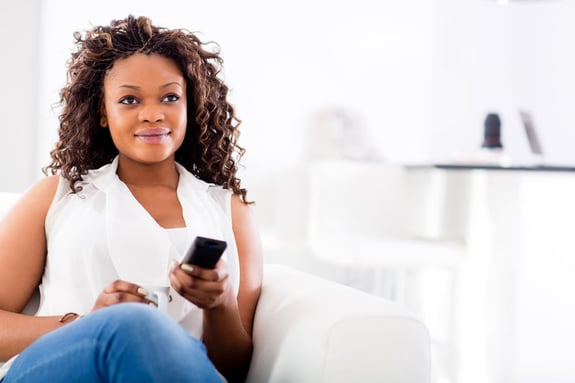 Woman watching tv at home and holding a remote control